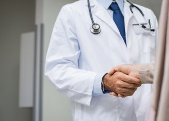 Doctor and patient at clinic shaking hands. Close up of a doctor man shaking hands with his woman patient. Male doctor and patient handshake closeup at the hospital.